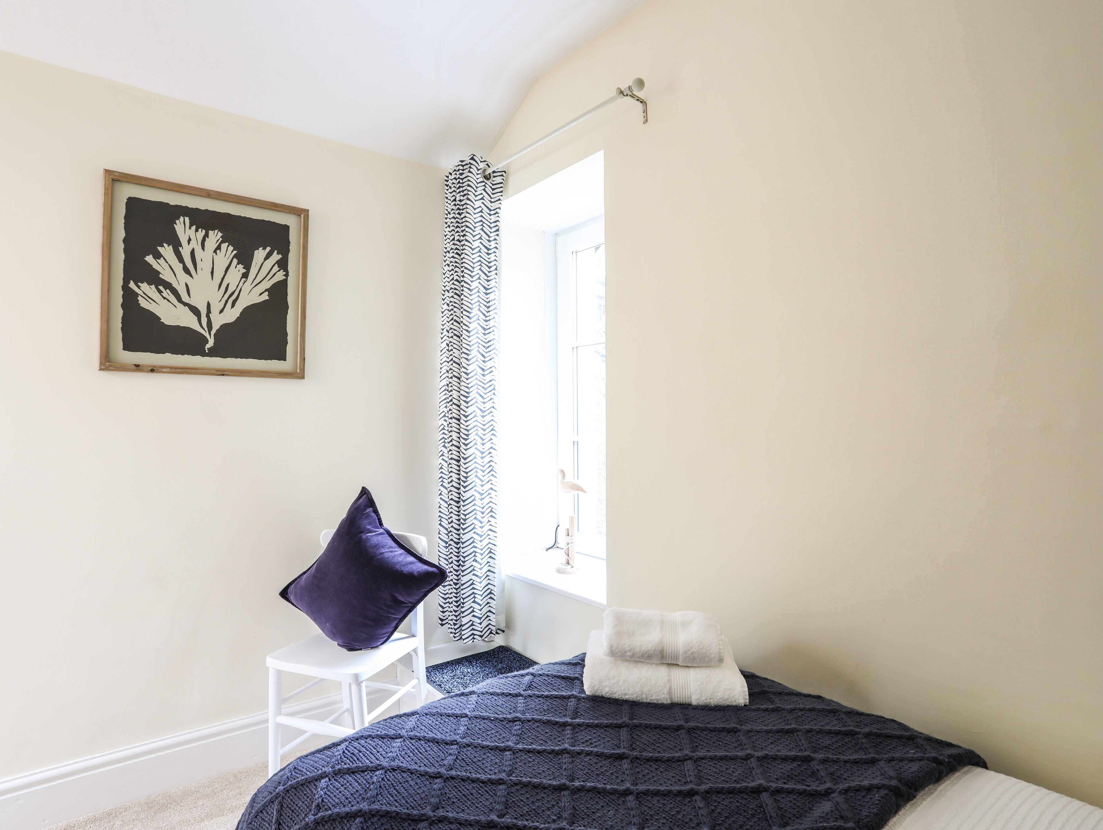 A bedroom with a bed, a chair, a window with a curtain, and a framed picture on the wall.