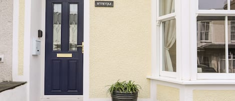 A front entrance with a dark blue door, a potted plant, and a sign reading "HYFRYDLE".