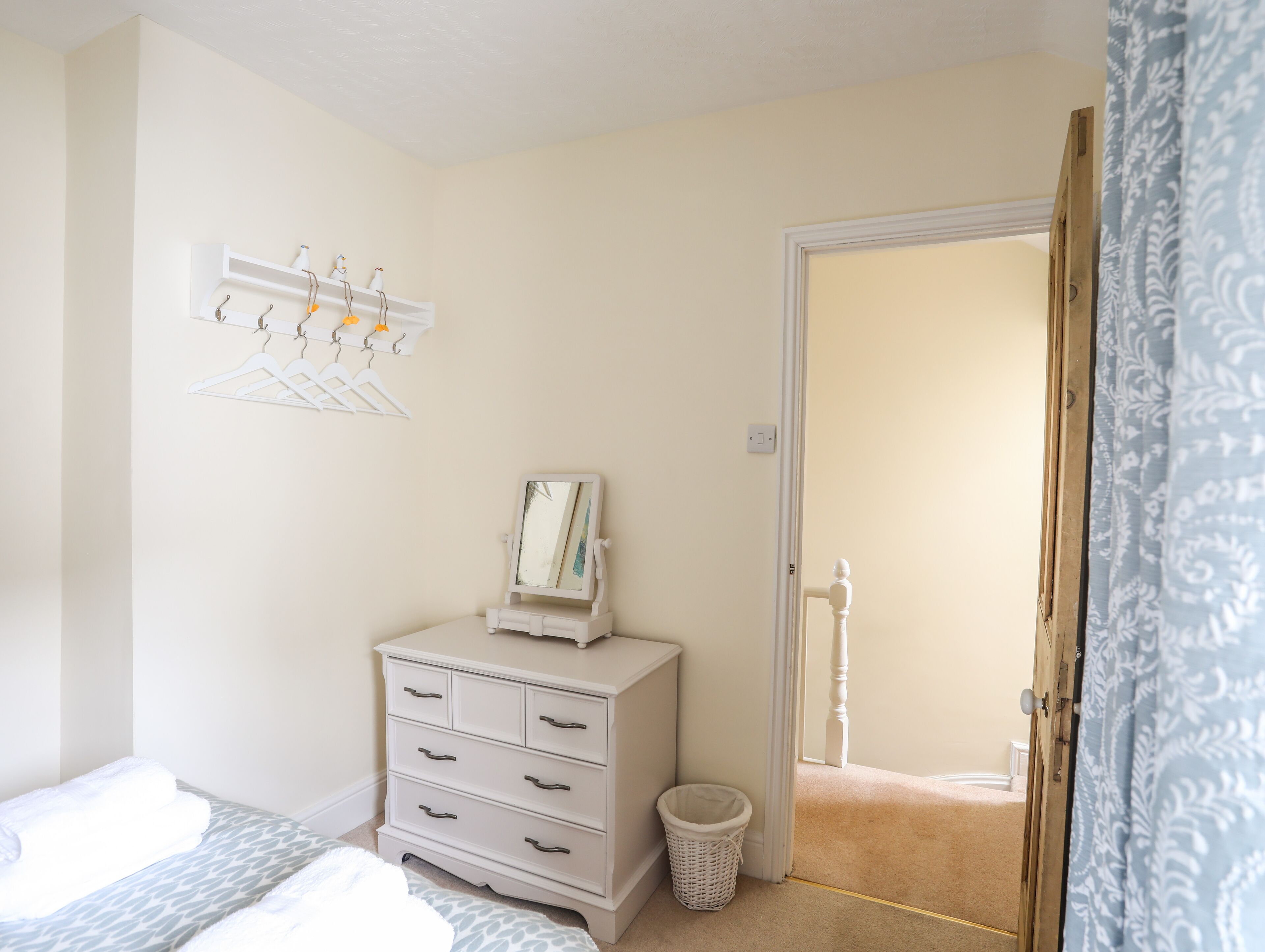 A bedroom with a bed, dresser, and a wall-mounted mirror. There is a door leading to another room.