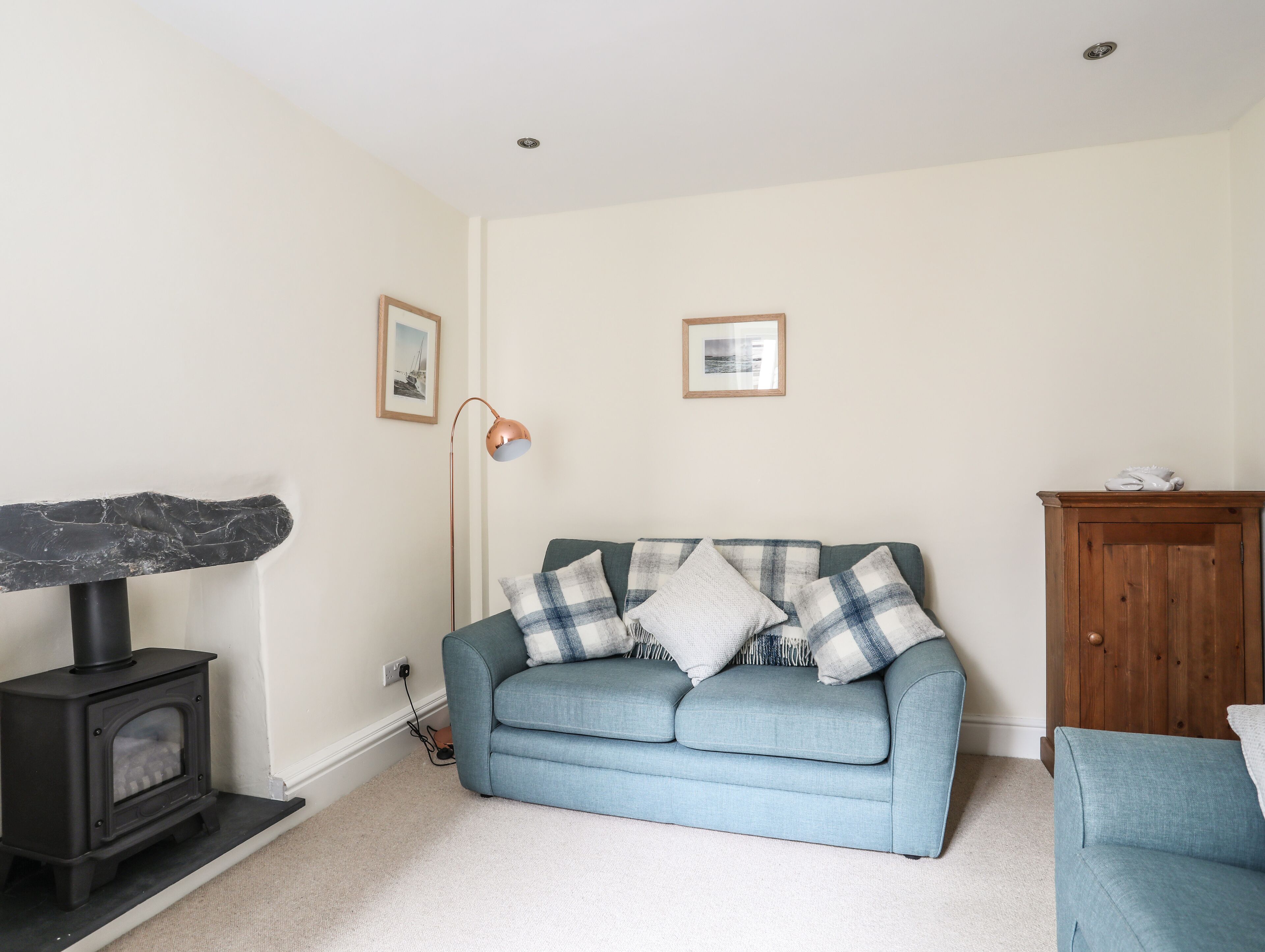 A living room with a blue sofa, a wooden cabinet, a black stove, and two framed pictures on the wall.
