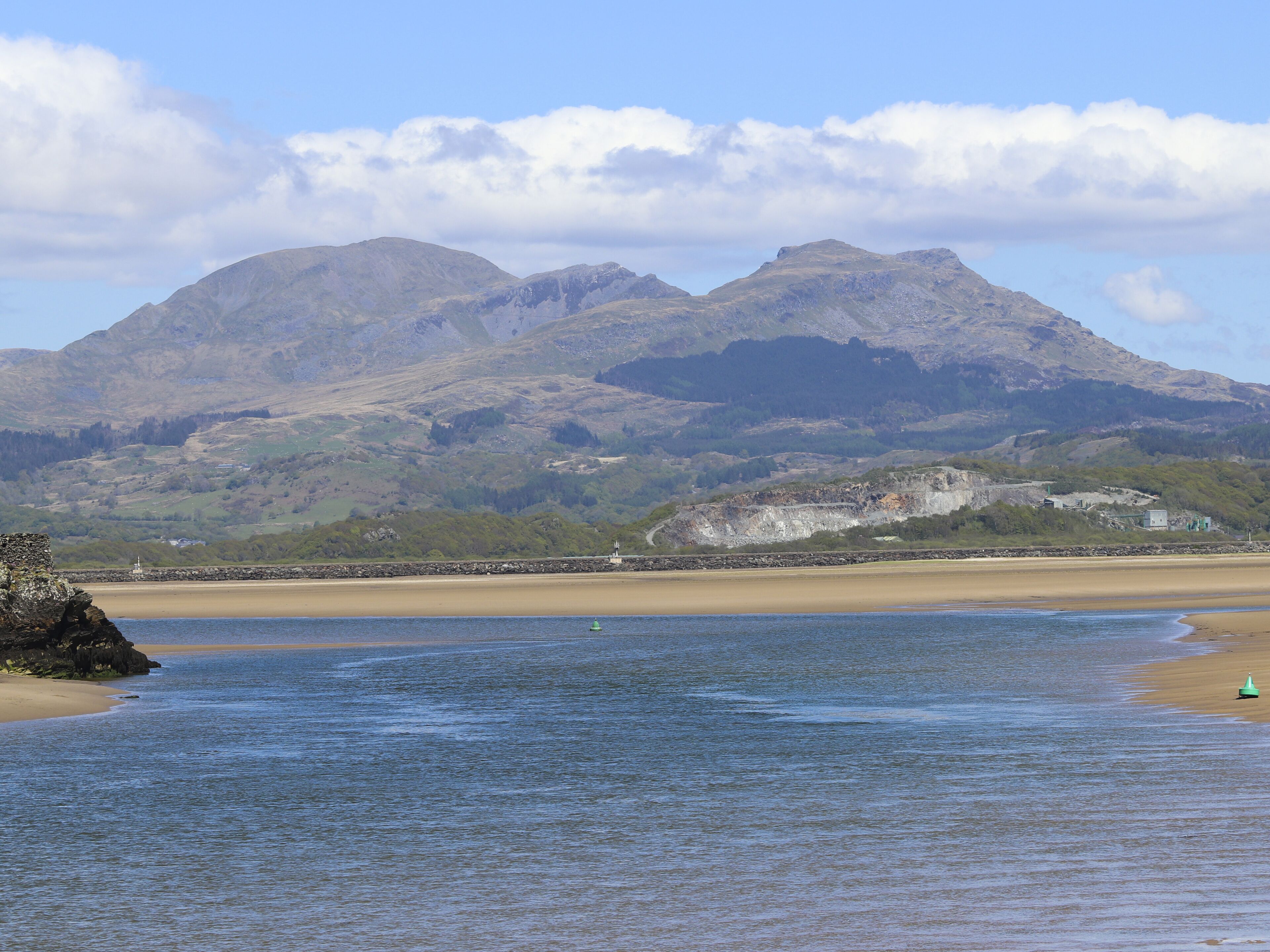 A coastal landscape with mountains in the background, a sandy beach, and a calm sea.