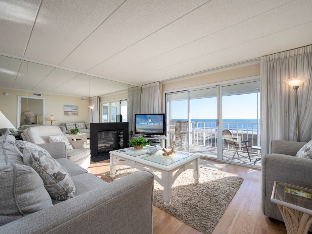 Un salón amplio con televisor, chimenea y balcón con vistas al mar.