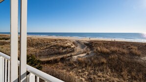 A view from a balcony overlooking a beach with a fence and dry grass. - Direct Oceanfront With a Pool! (Ocean City)