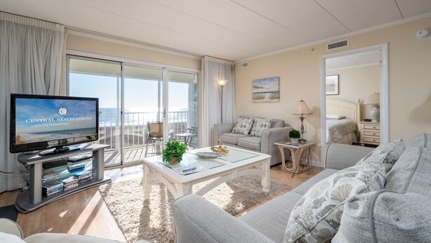 A spacious living room with a large television, a balcony with a view, and a cozy seating area. - Direct Oceanfront With a Pool! (Ocean City)