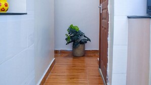 A narrow hallway with white tiled walls and a wooden floor. A potted plant is placed against the wall, and a door is visible on the right. - Dream house (Nairobi)