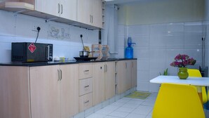 A kitchen with light wooden cabinets, a microwave, a gas stove, a sink, and a yellow table with a vase. - Dream house (Nairobi)