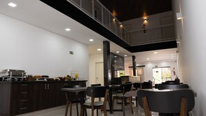 A modern hotel kitchen with a dining area, featuring a buffet setup, a reception desk, and a staircase leading to an upper level.