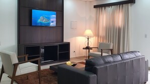 A modern living room with a flat-screen TV mounted on a dark wooden panel, a grey leather sofa, a brown rug, a lamp, and a chair.