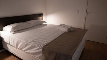 Ein ordentlich bezogenes Bett mit weißen Leinentüchern und einer braunen Tagesdecke, eine Nachttischlampe und eine geschlossene Tür in einem Hotelzimmer.