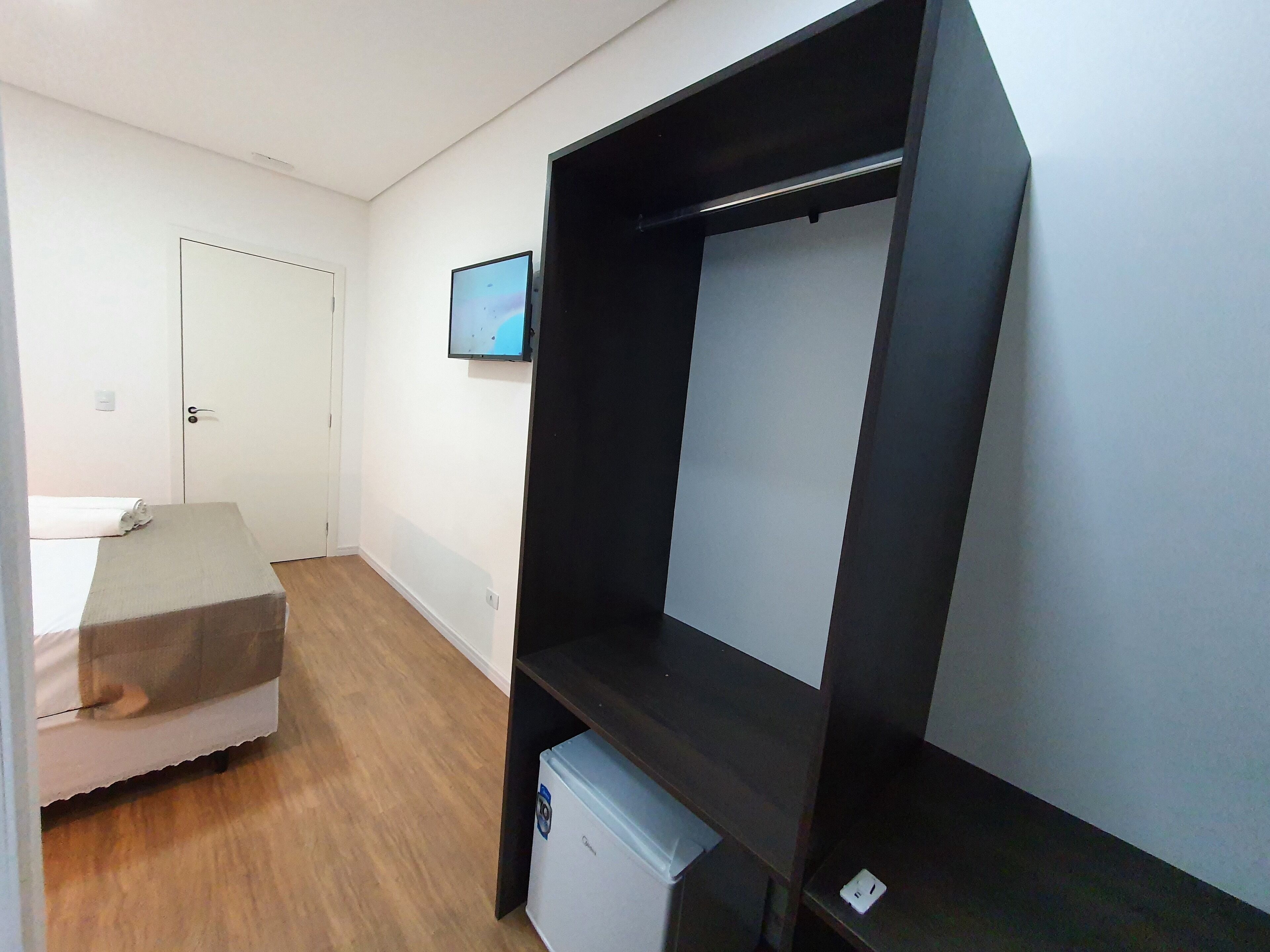 Una habitación con una cama, una mesita, un televisor en la pared y un armario.