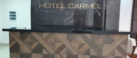 A reception desk with a marble top and geometric patterned base, labeled "HOTEL CARMEL."