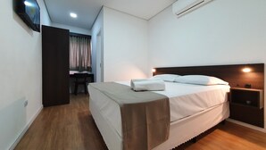 A hotel room with a bed, a desk, a chair, an air conditioning unit, and a television mounted on the wall.
