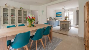 A spacious dining area with a wooden table and teal chairs, a kitchen with a view, and a large cabinet with glass doors. - The Broadstairs Townhouse (Broadstairs)