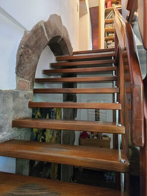 A wooden staircase with a stone archway leading to a room with a wooden dresser and a red hat on it.