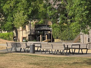 Un parque con bancos, un bote de basura y juegos infantiles.
