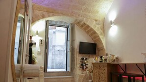 Une pièce chaleureuse avec une arche en pierre, un téléviseur fixé au mur, un petit coin bar et une fenêtre donnant sur la rue.