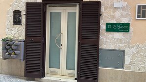Une entrée d’immeuble avec une façade en pierre, une porte dotée d’un panneau en verre dépoli et une enseigne indiquant « Le Gemelle », avec un numéro de téléphone.