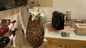Une petite table sur laquelle se trouvent une machine à café, un vase avec des fleurs et une boîte de tasses à café.