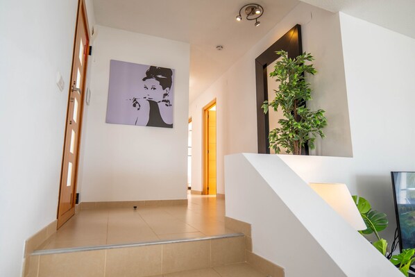 A modern interior with a staircase, a framed artwork on the wall, and a potted plant.