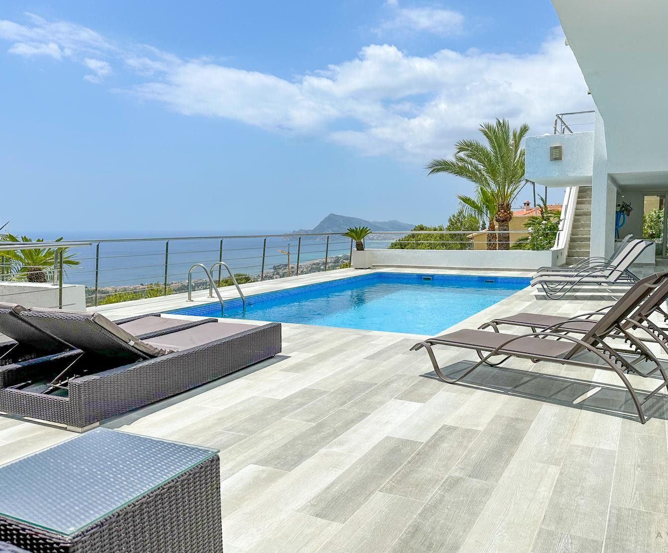 A rooftop pool with a view of the sea, lounge chairs, and a staircase leading to an upper level.