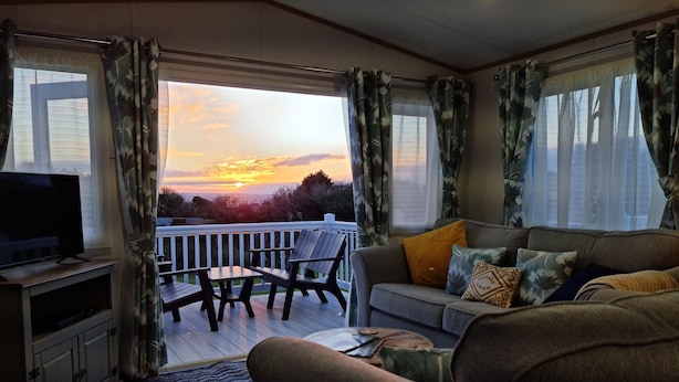 Uma sala de estar com sofá, televisão e varanda com vista para o pôr do sol.