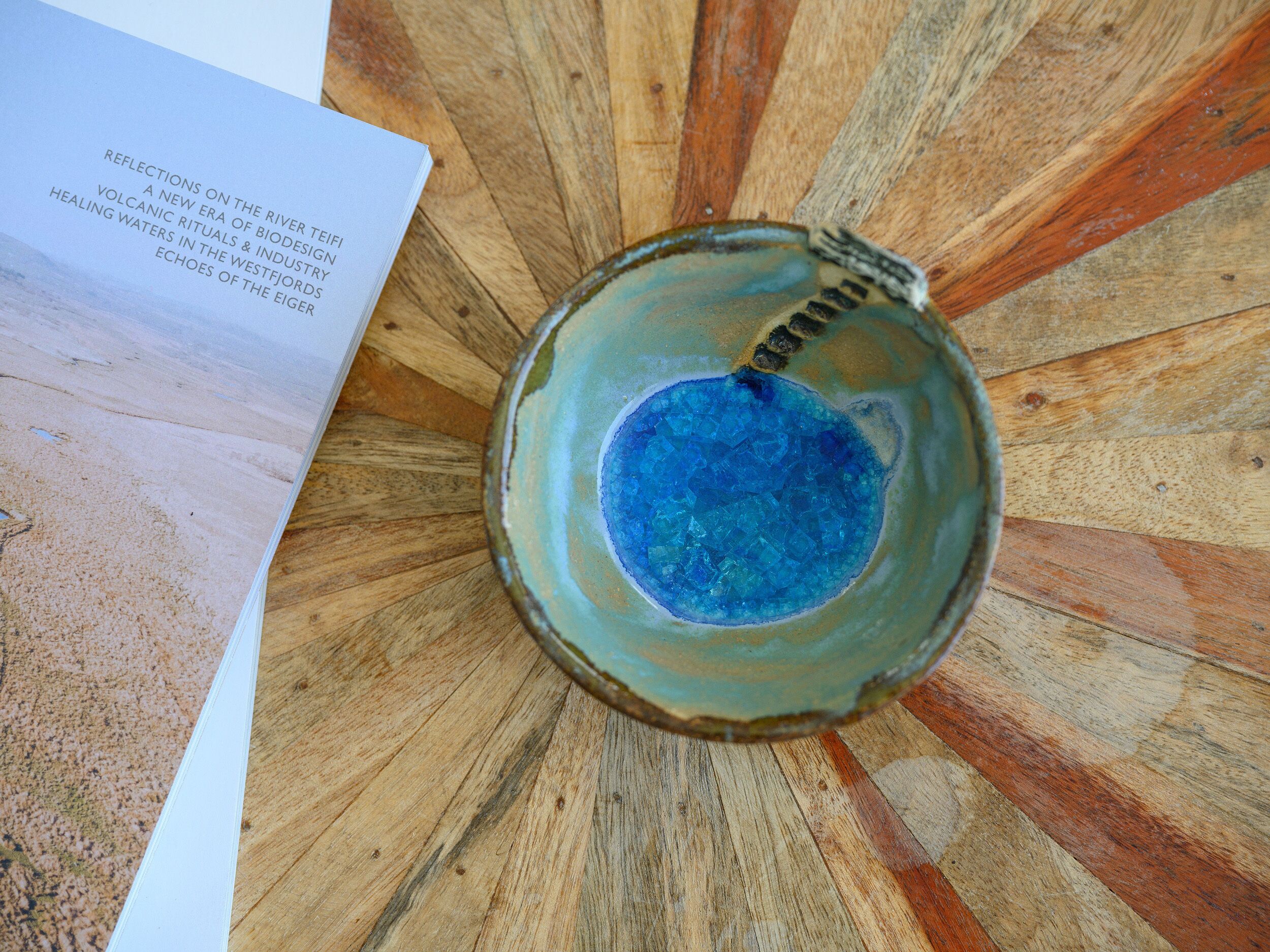 A ceramic bowl with a blue interior, placed on a wooden surface with a book beside it.