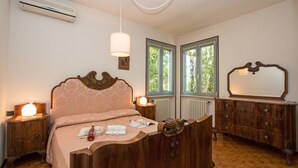 Un dormitorio con cama de madera, lámparas de noche, cómoda y ventana con vista a árboles.