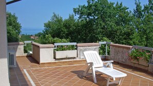 Una terraza con una silla blanca, una mesita y una jardinera con flores.