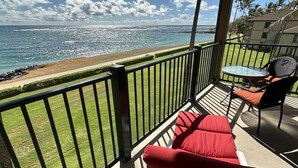 A balcony with a view of the ocean, a table with chairs, and red cushions. - Unbeatable Ocean Front Condo  Pono Kai Resort C302 (Kapa'a)