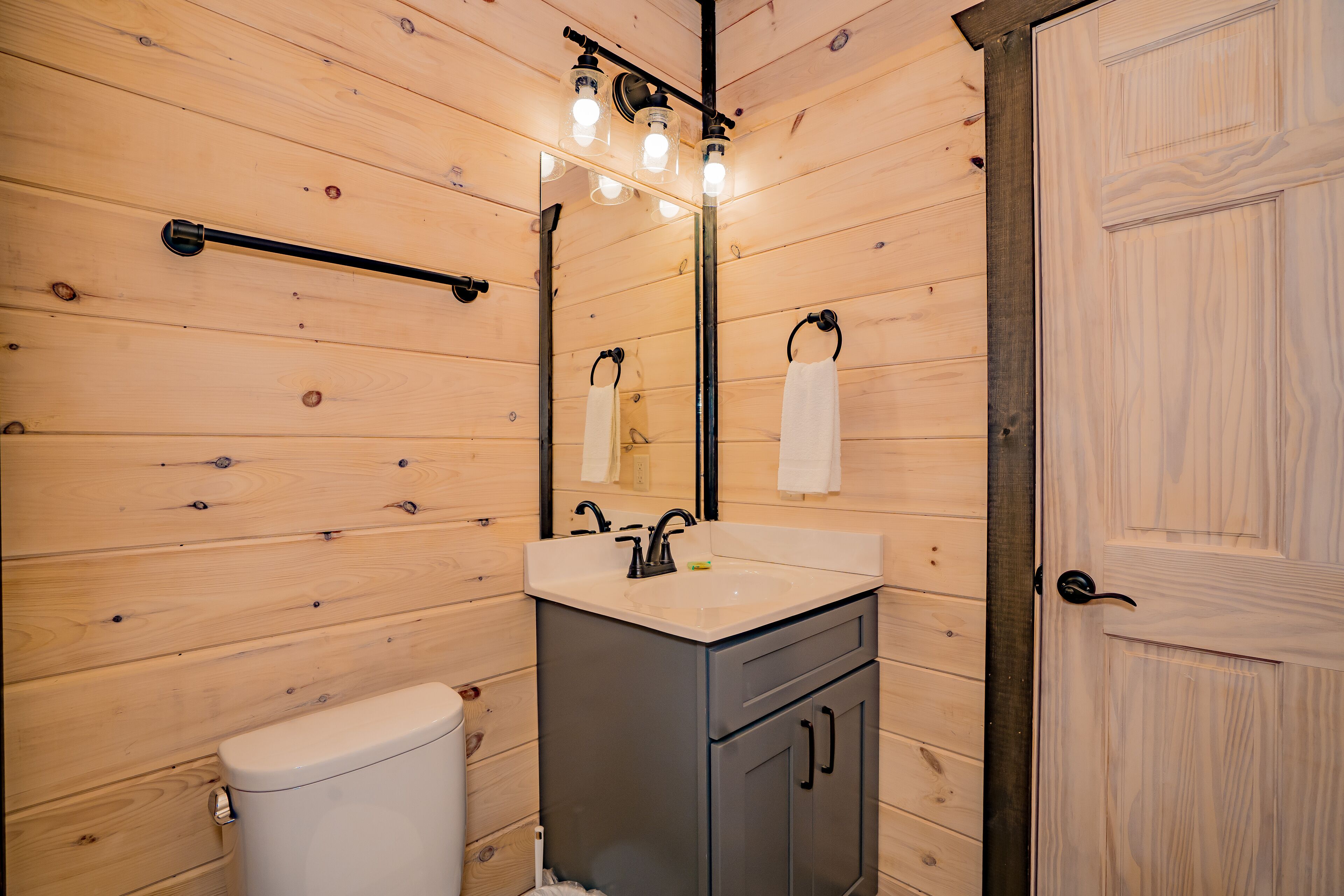 Ein Badezimmer mit Holzwandverkleidung, Toilette, Waschbecken, Spiegel und Handtuchhalter.