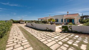 A paved pathway leading to a white building with a red-tiled roof, surrounded by greenery and a clear blue sky.