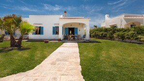 A white building with blue shutters and a stone pathway leading to a patio area.