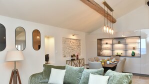 Ein modernes Wohnzimmer mit einem grünen Sofa, einem Essbereich mit Tisch und Stühlen sowie einer Küche mit integriertem Regal.