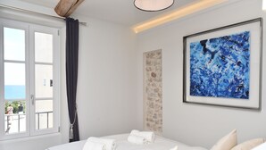 Ein Hotelzimmer mit Bett, großem Fenster, Steinwand und einem gerahmten abstrakten Gemälde.