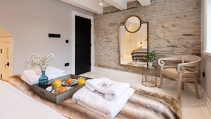Une chambre d’hôtel moderne avec un mur en pierre, un grand miroir, une chaise en bois et un plateau de petit-déjeuner sur le lit.