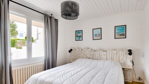 Une chambre avec un grand lit, une fenêtre avec des rideaux, un radiateur et trois tableaux encadrés accrochés au mur.