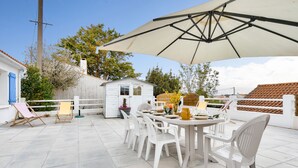 Une terrasse extérieure avec une table et des chaises, un petit abri de jardin et un grand parasol.
