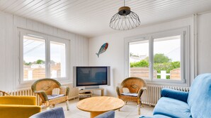 Un salon avec un téléviseur, des meubles en osier, un canapé bleu et de grandes fenêtres.