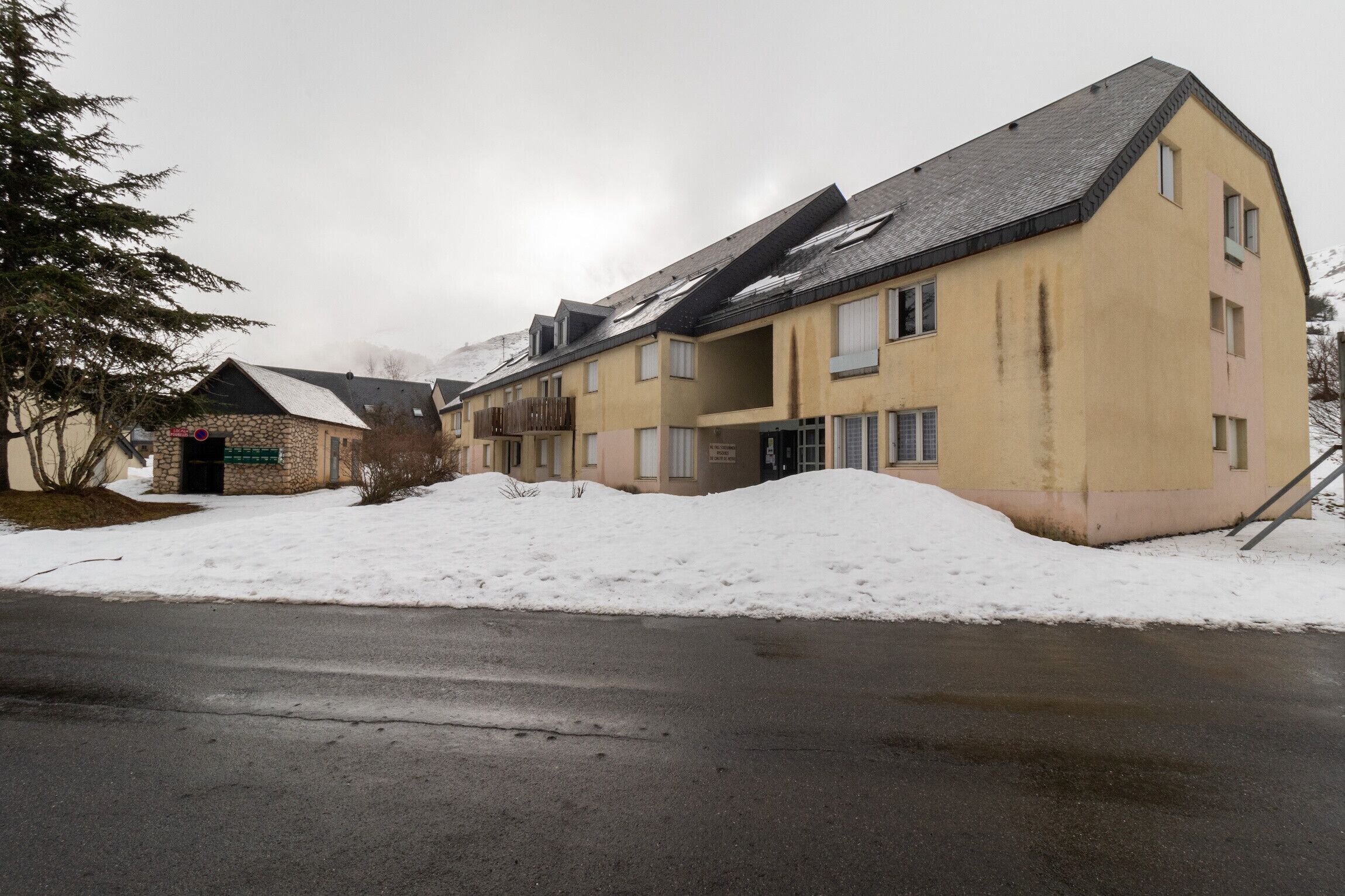 A multi-story building with a sloped roof, a stone facade, and a snow-covered ground.