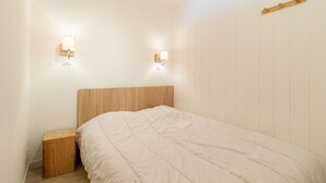 Un dormitorio con cabecera de madera, cubrecama blanco y dos lámparas fijadas a la pared.