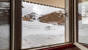 Vista a través de una ventana que muestra un paisaje nevado con una valla de madera y una colina.