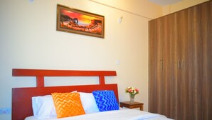 A bedroom with a bed, a wooden wardrobe, a nightstand with a vase of flowers, and a painting on the wall. - Mukoma Heights (Nairobi)