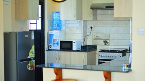 A kitchen with a refrigerator, microwave, water dispenser, and a small countertop with a chair. - Mukoma Heights (Nairobi)