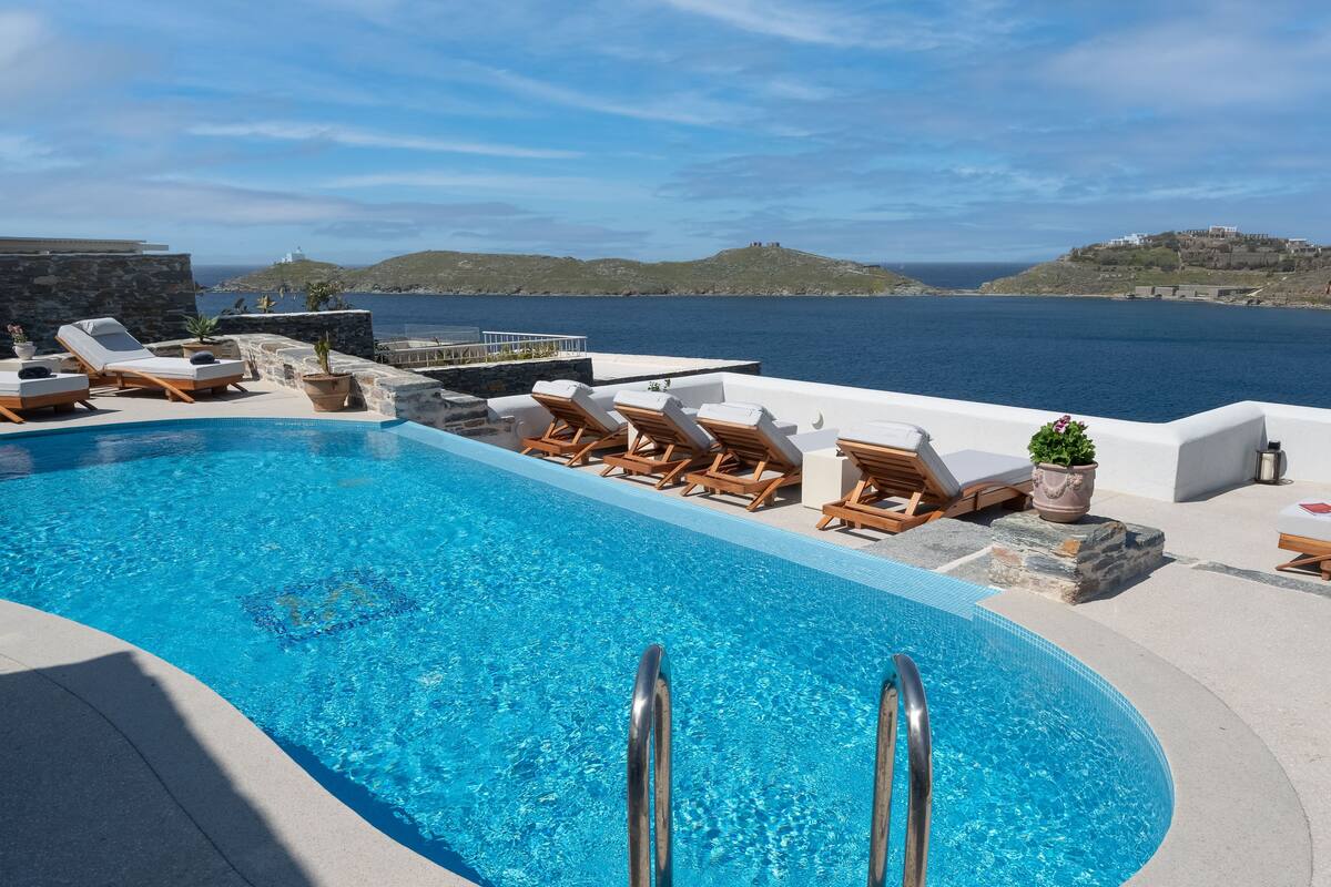A pool area with lounge chairs and a view of the sea.