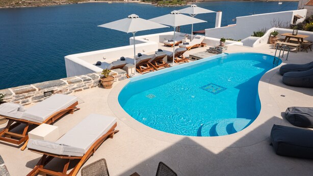 A pool area with lounge chairs and umbrellas, overlooking a body of water and a hilly landscape. - KEA MARE LUXURY VILLAS (Kea)