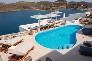 A pool area with lounge chairs and umbrellas, overlooking a body of water and a hilly landscape. - KEA MARE LUXURY VILLAS (Kea)