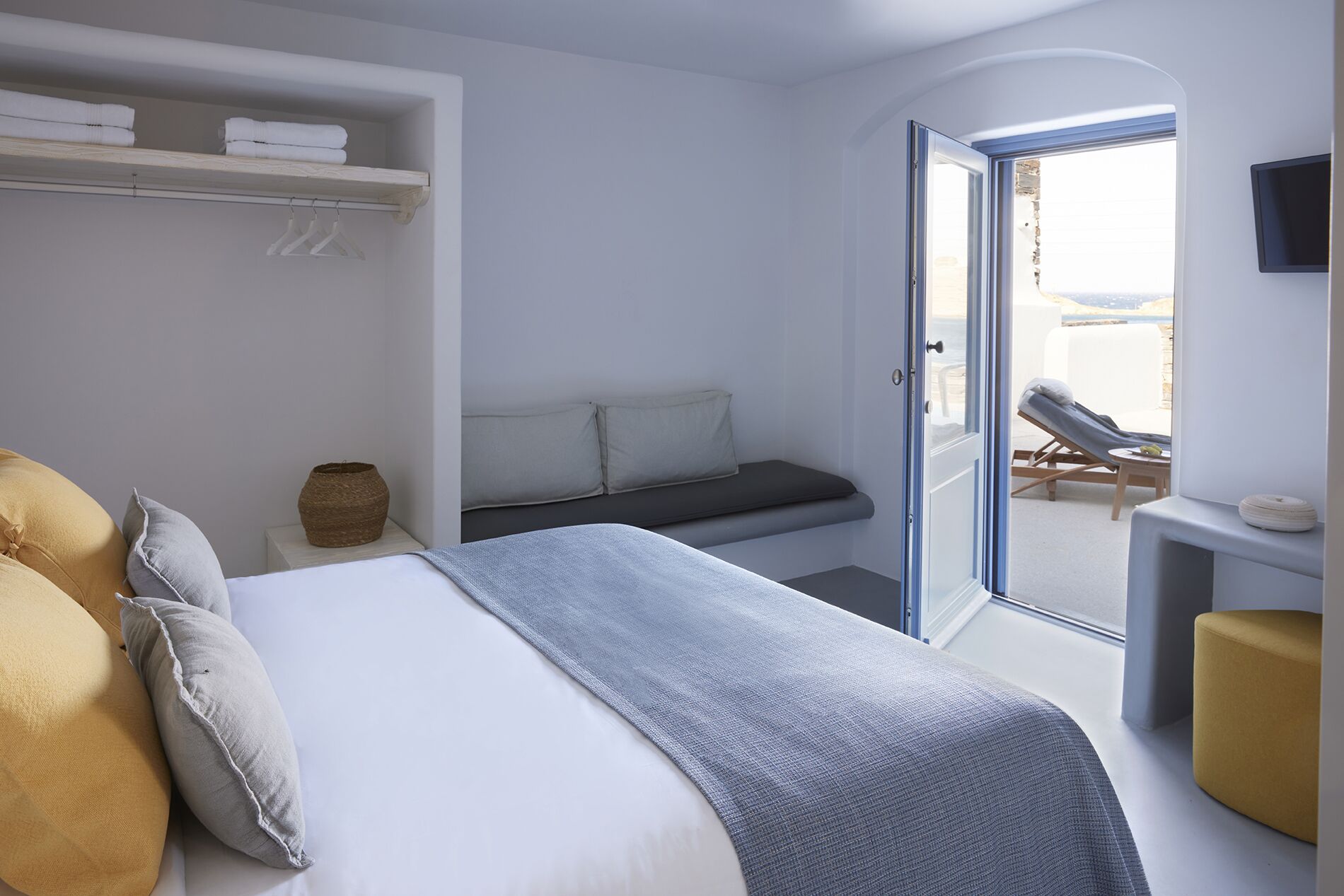 A bedroom with a bed, a bench, a TV, and a view of the beach.