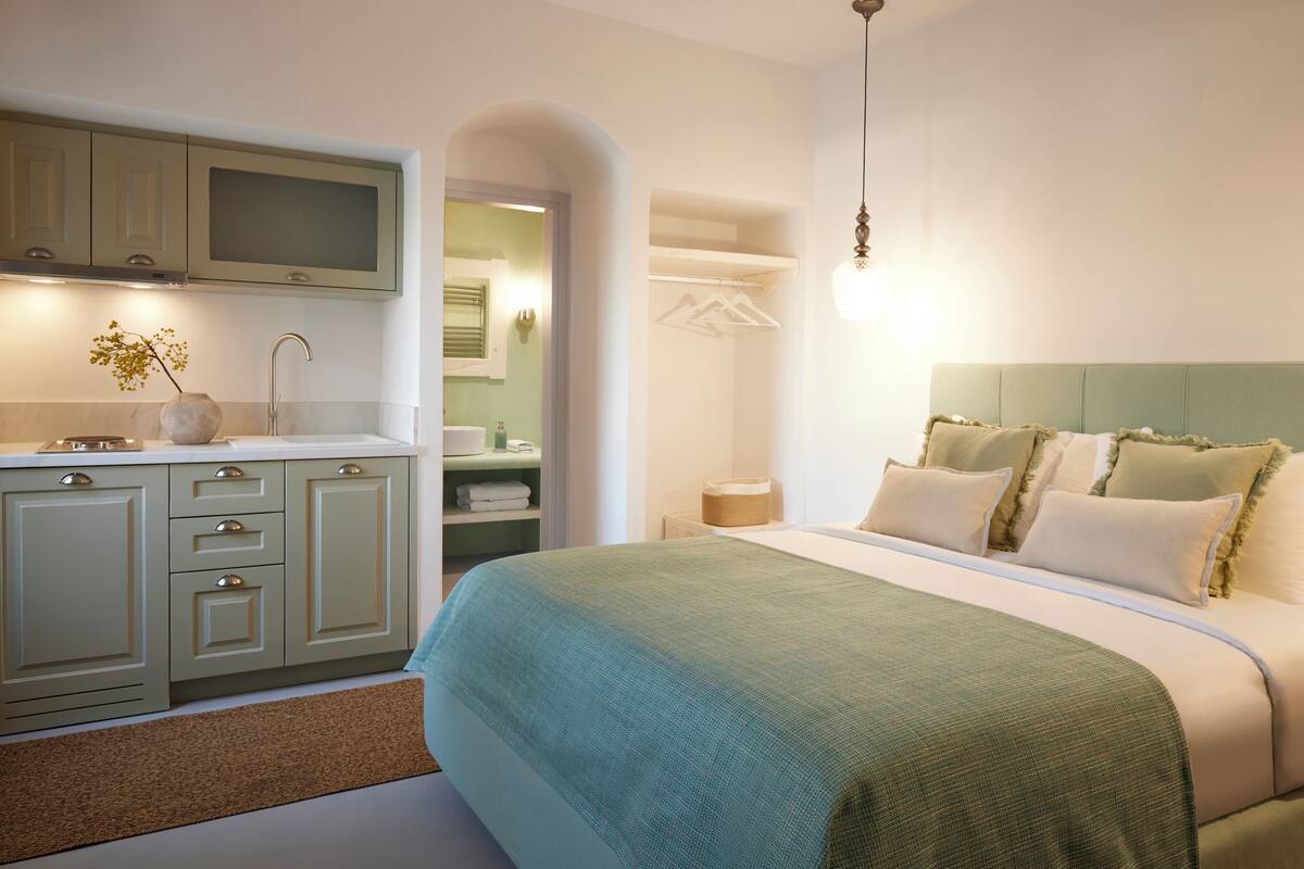 A bedroom with a large bed, a nightstand, and a dresser. There is a bathroom visible through an archway.