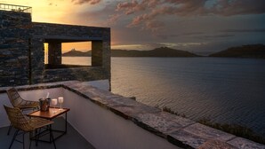 A terrace with a table and chairs overlooking a body of water, with stone walls and a view of distant hills. - KEA MARE LUXURY VILLAS (Kea)