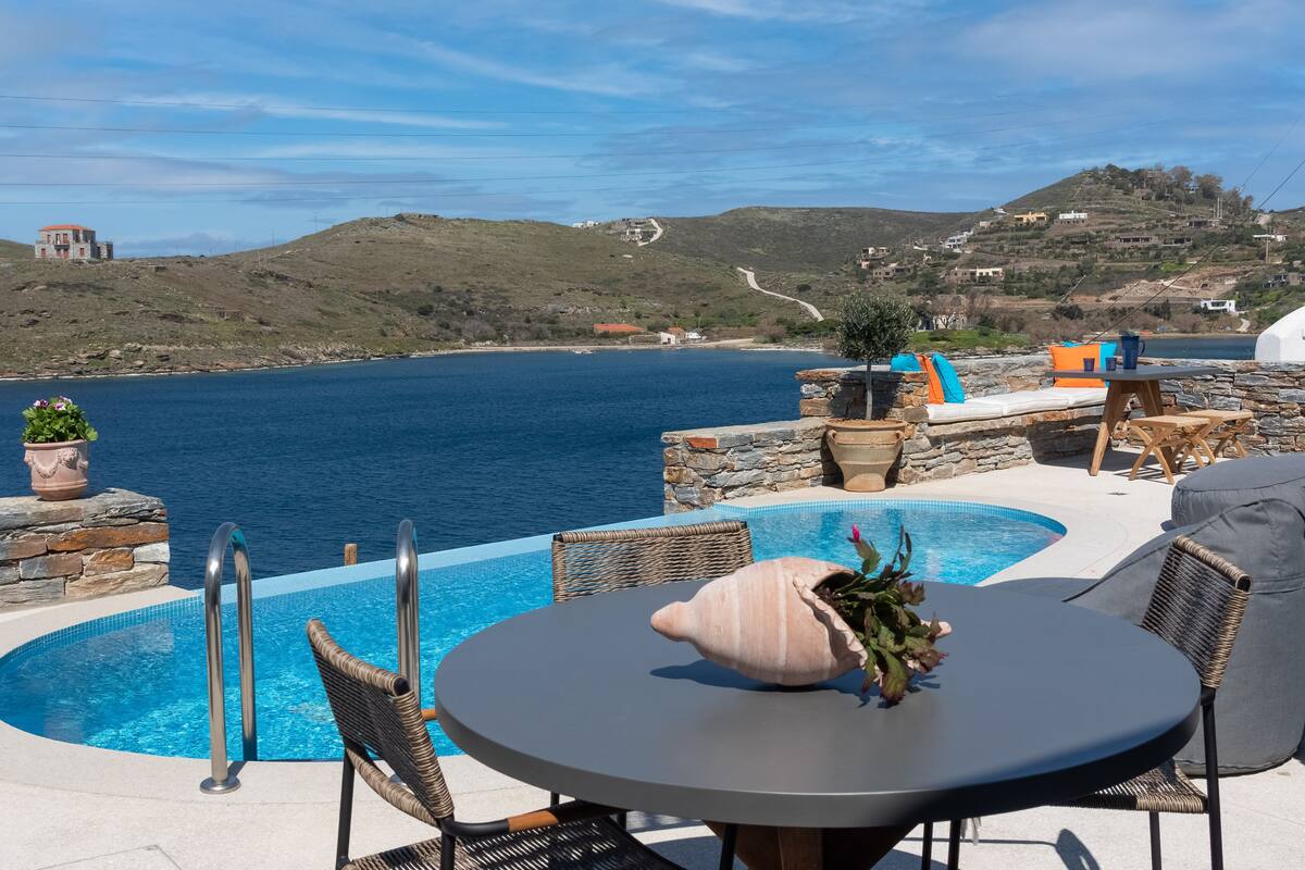 An outdoor infinity pool with a view of the sea, surrounded by stone walls and wicker furniture.